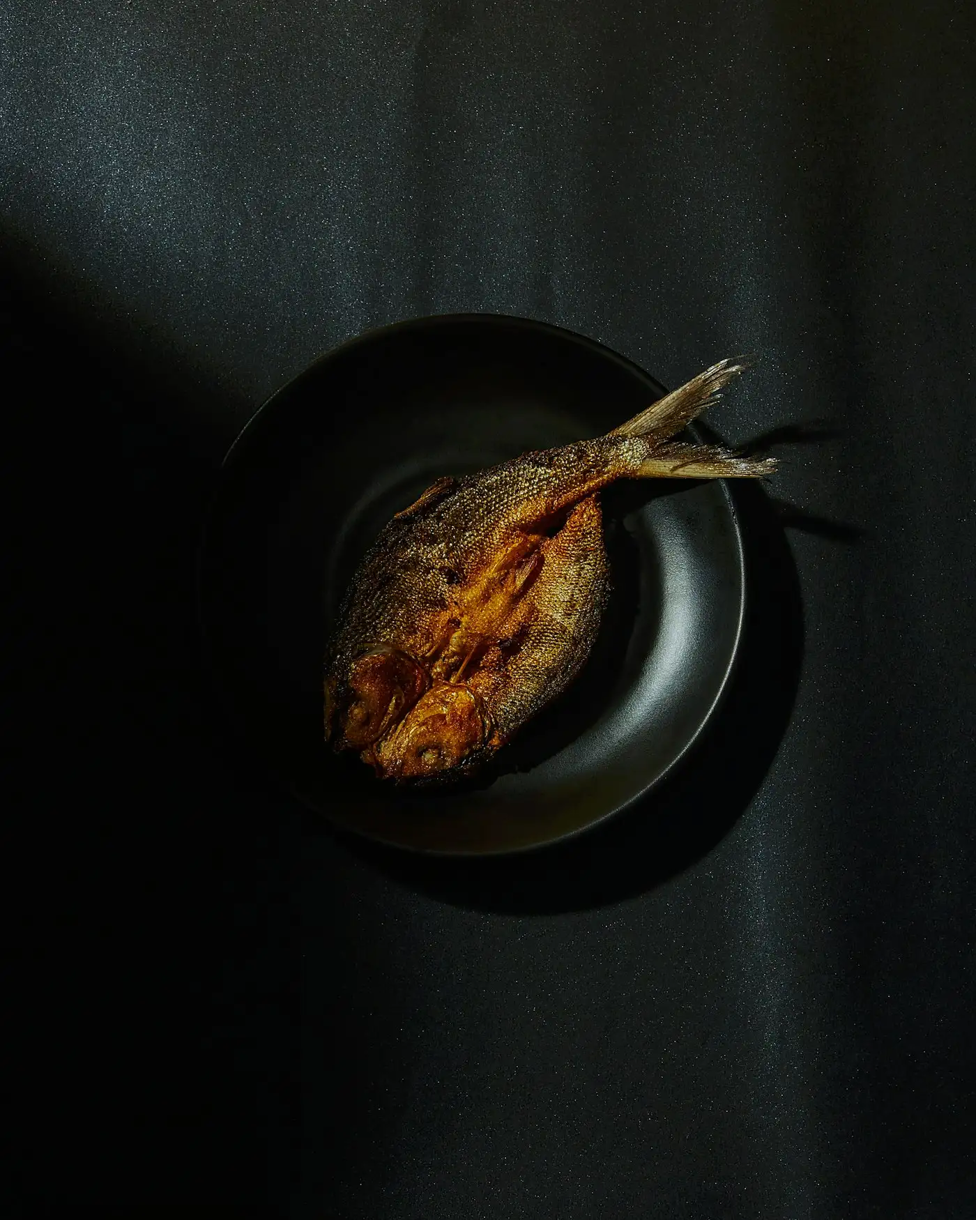 Whole fried fish on a black plate